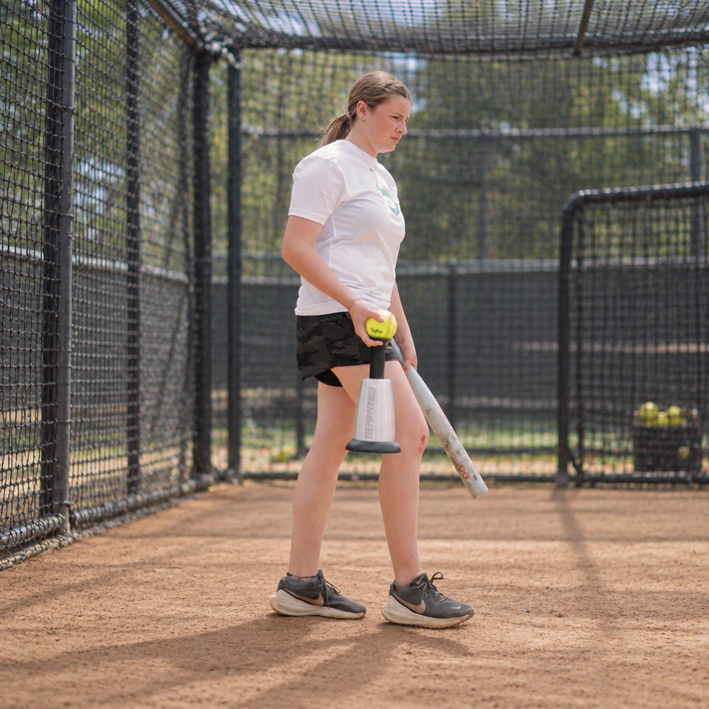 A softball player carries the Tee Popper Pro into a batting cage